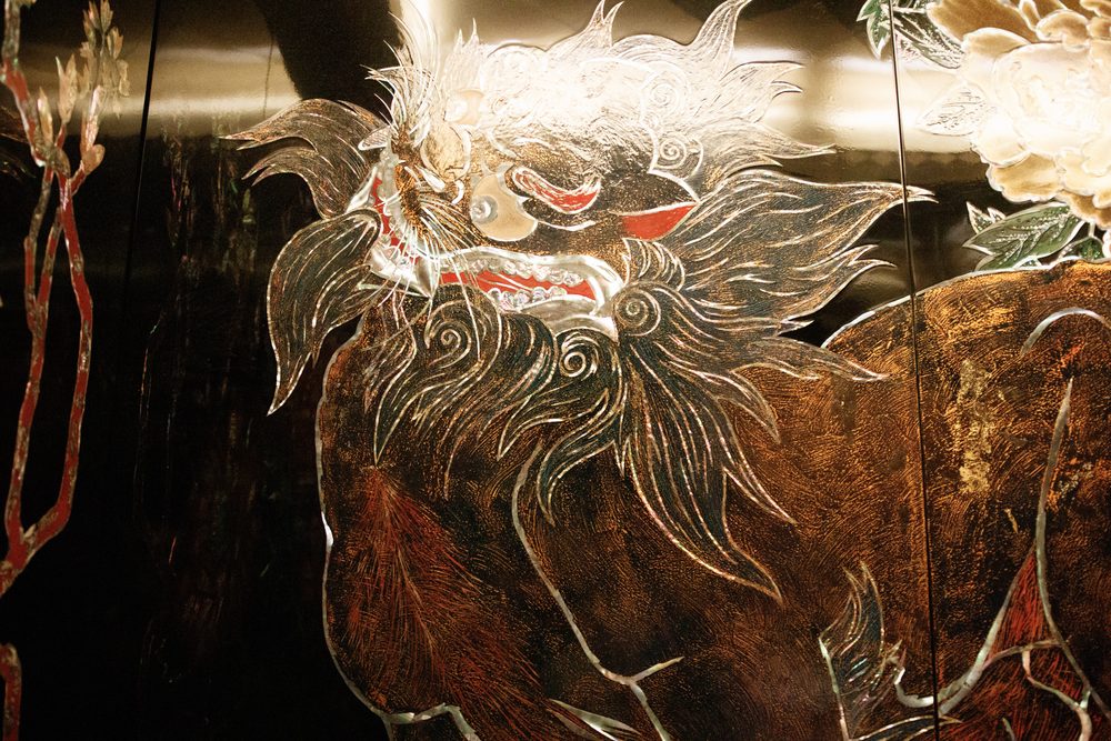 A shishi lion with a swirling white mane picked out in mother-of-pearl on a dark lacquer panel