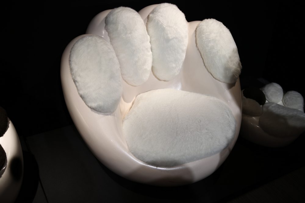 A white chair shaped like a giant cat's paw, with soft grey pads, under a spotlight