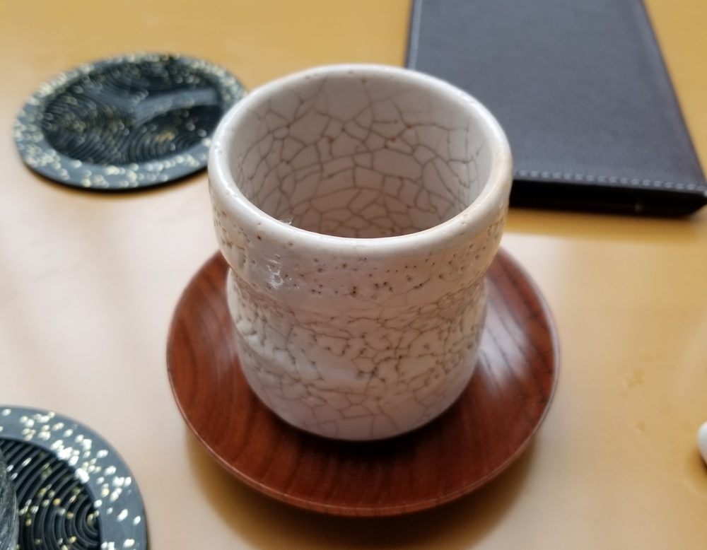 A crackle-glazed teacup on a red lacquered saucer on a pale wooden table