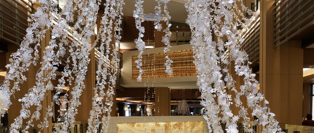 Strands of white paper snowflake decorations hanging through a multi-level wood-panelled shopping atrium