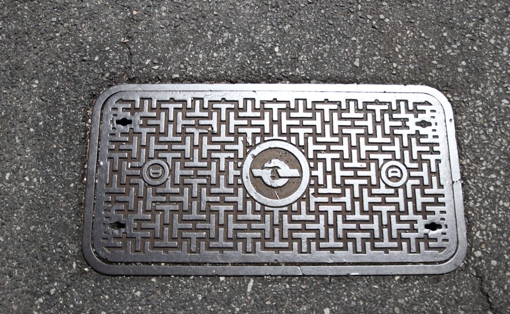 A cast-iron utility cover with a fret pattern set into a country road in the Kumano hills